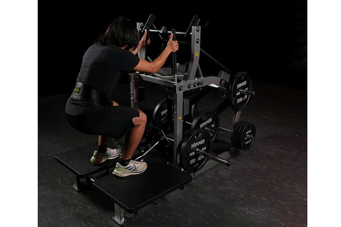 Person in black shirt performing squat exercise on Hammer Strength plate-loaded belt squat machine with weight plates loaded 