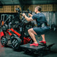 Man performing leg exercise on black and red plate-loaded belt squat machine in gym setting