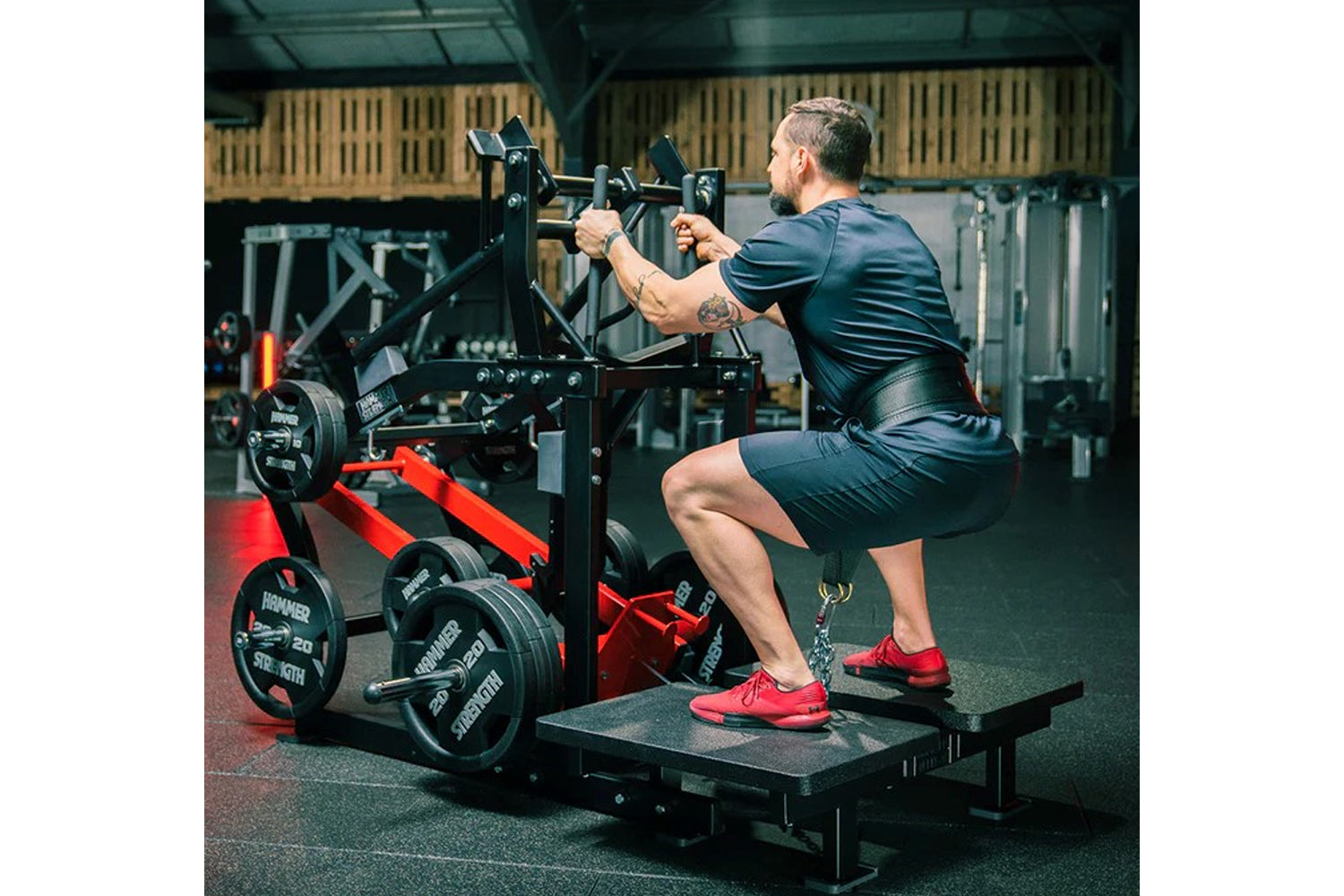 Man performing leg exercise on black and red plate-loaded belt squat machine in gym setting