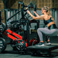 Woman using black and red Hammer Strength plate-loaded belt squat machine in gym, wearing black sports bra and gray leggings