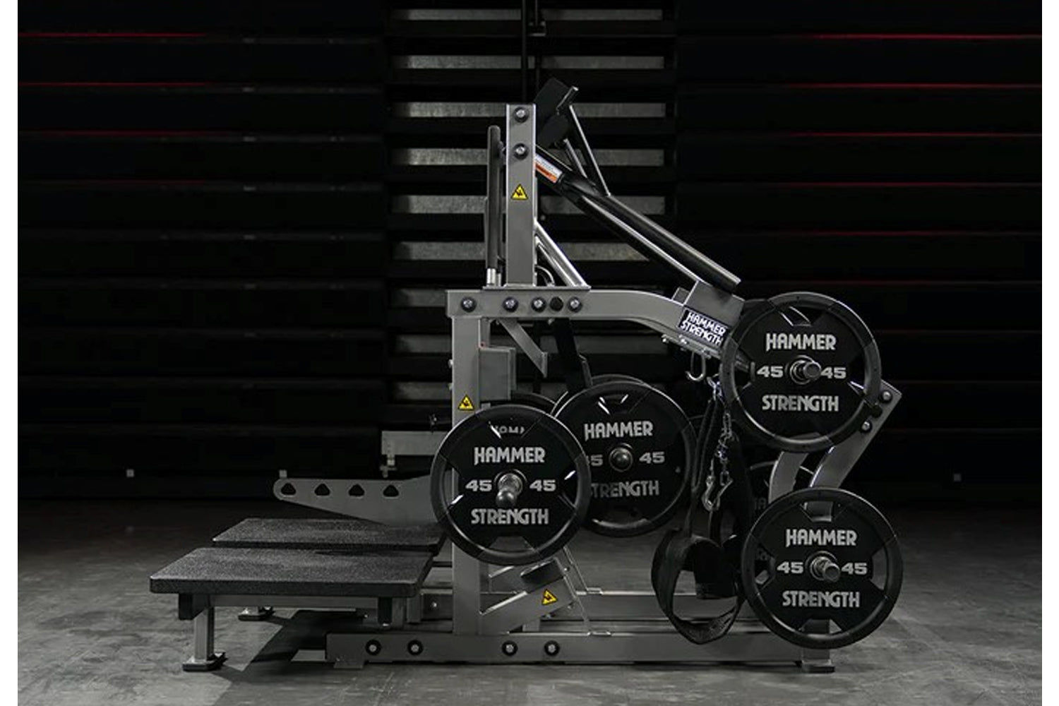 Hammer Strength plate-loaded belt squat machine with gray steel frame, black weight plates labeled 45, and integrated bench o