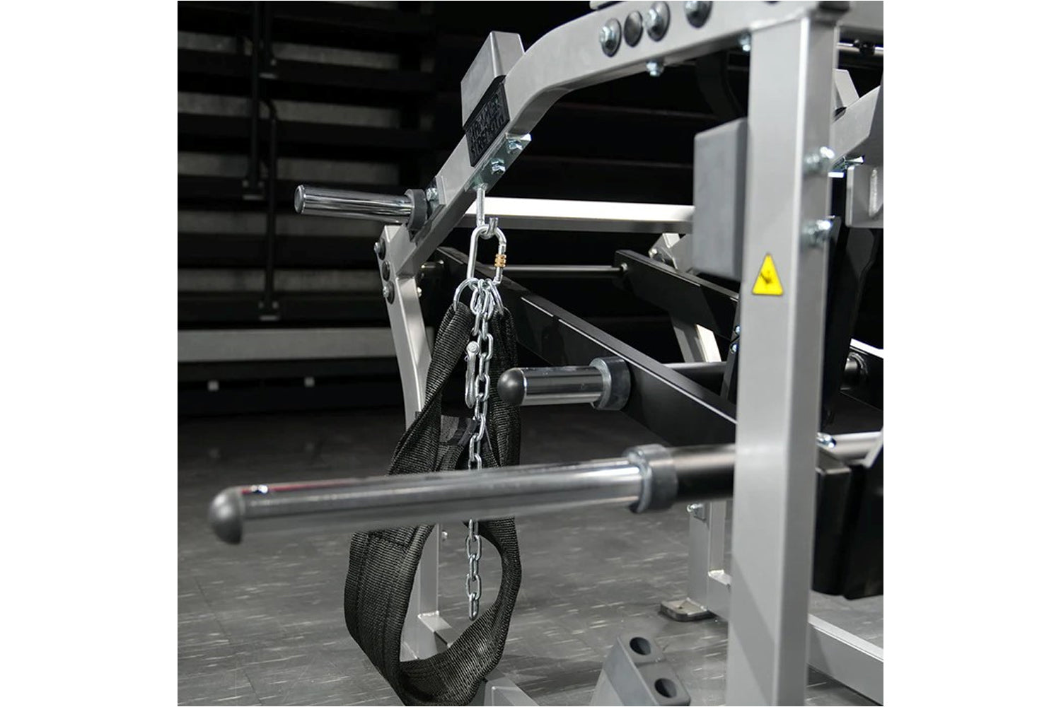 Hammer Strength plate-loaded belt squat machine with gray frame, black straps, and chain attachment in gym setting