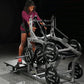 Woman in burgundy hoodie and black shorts using silver and black Hammer Strength plate-loaded belt squat machine in gym setti