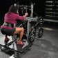 Woman using black Hammer Strength plate-loaded belt squat machine in gym setting, wearing magenta long-sleeve top and black s