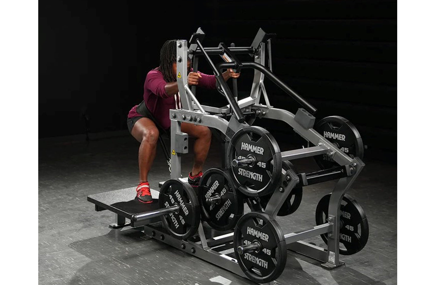 Woman in burgundy shirt using silver and black Hammer Strength plate-loaded belt squat machine with weight plates loaded