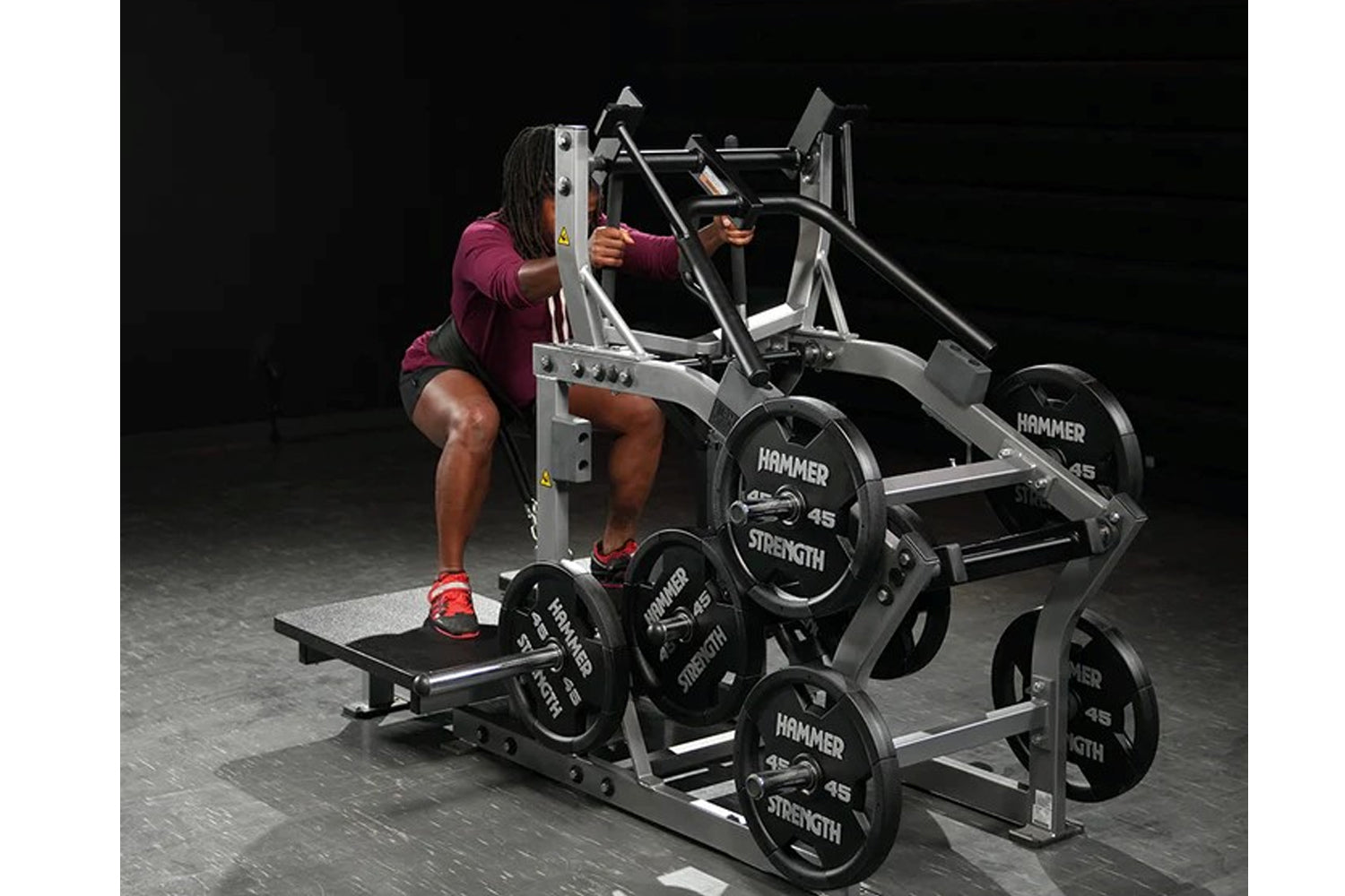 Woman in burgundy shirt using silver and black Hammer Strength plate-loaded belt squat machine with weight plates loaded