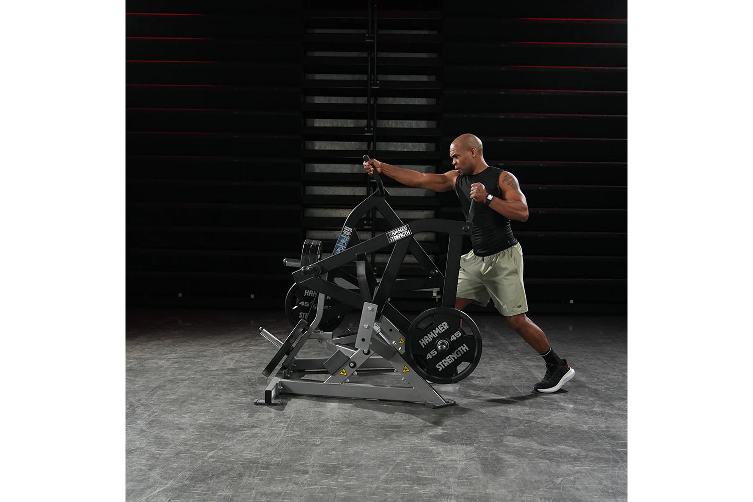 Man wearing black sleeveless tank and beige shorts using Hammer Strength plate-loaded combo twist machine in gym setting