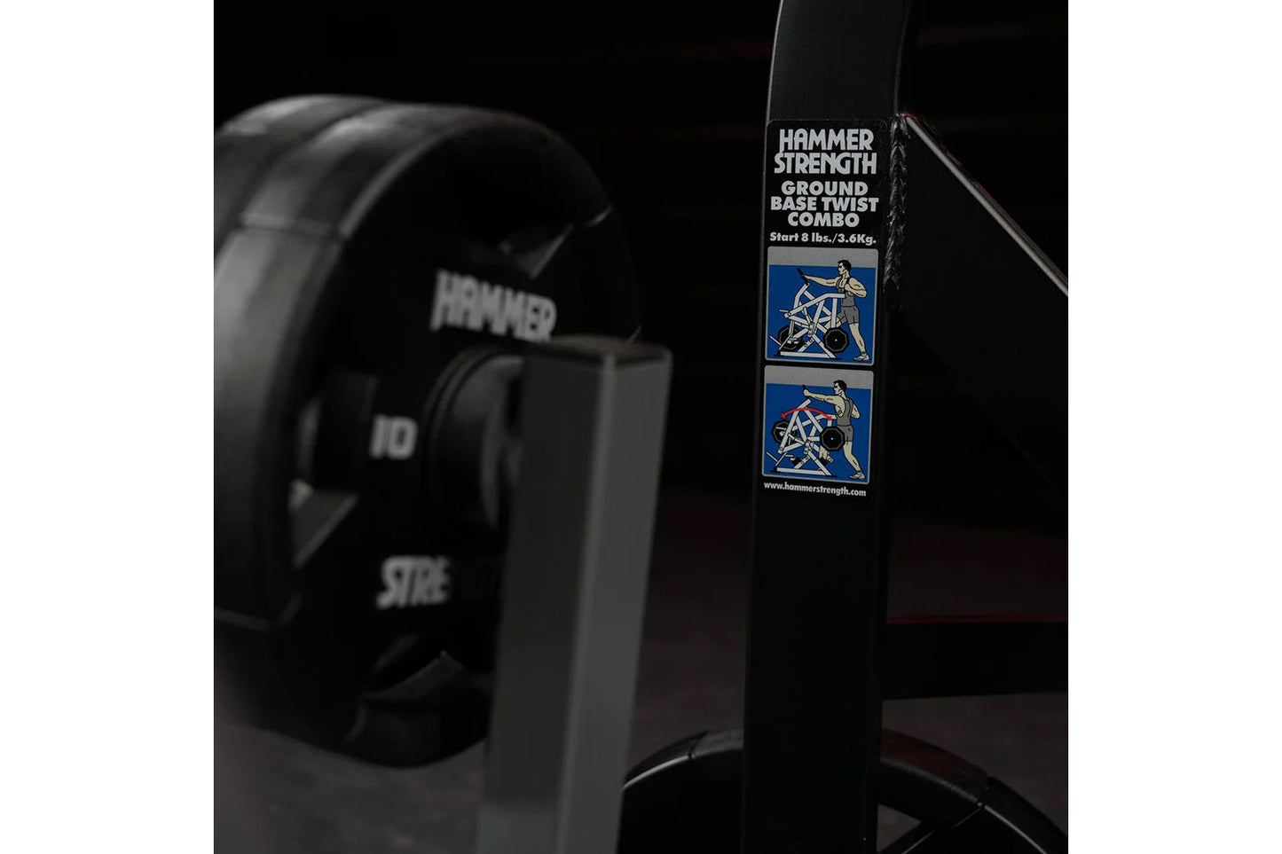 Hammer Strength ground base twist combo plate-loaded machine with dual blue illustration badges on black frame against dark b
