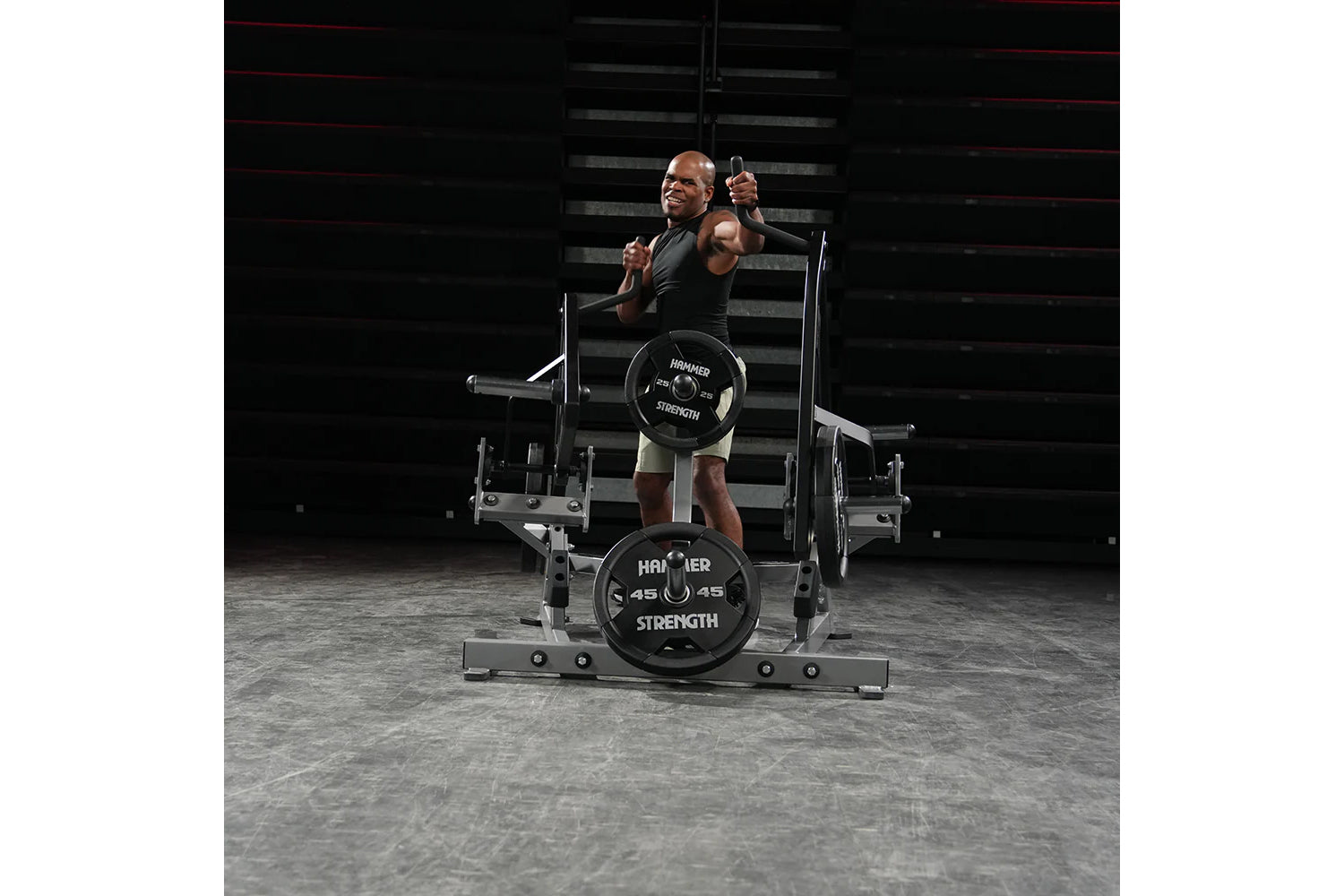 Man in black sleeveless shirt performing squat on Hammer Strength plate-loaded machine with 45-pound weights loaded, industri