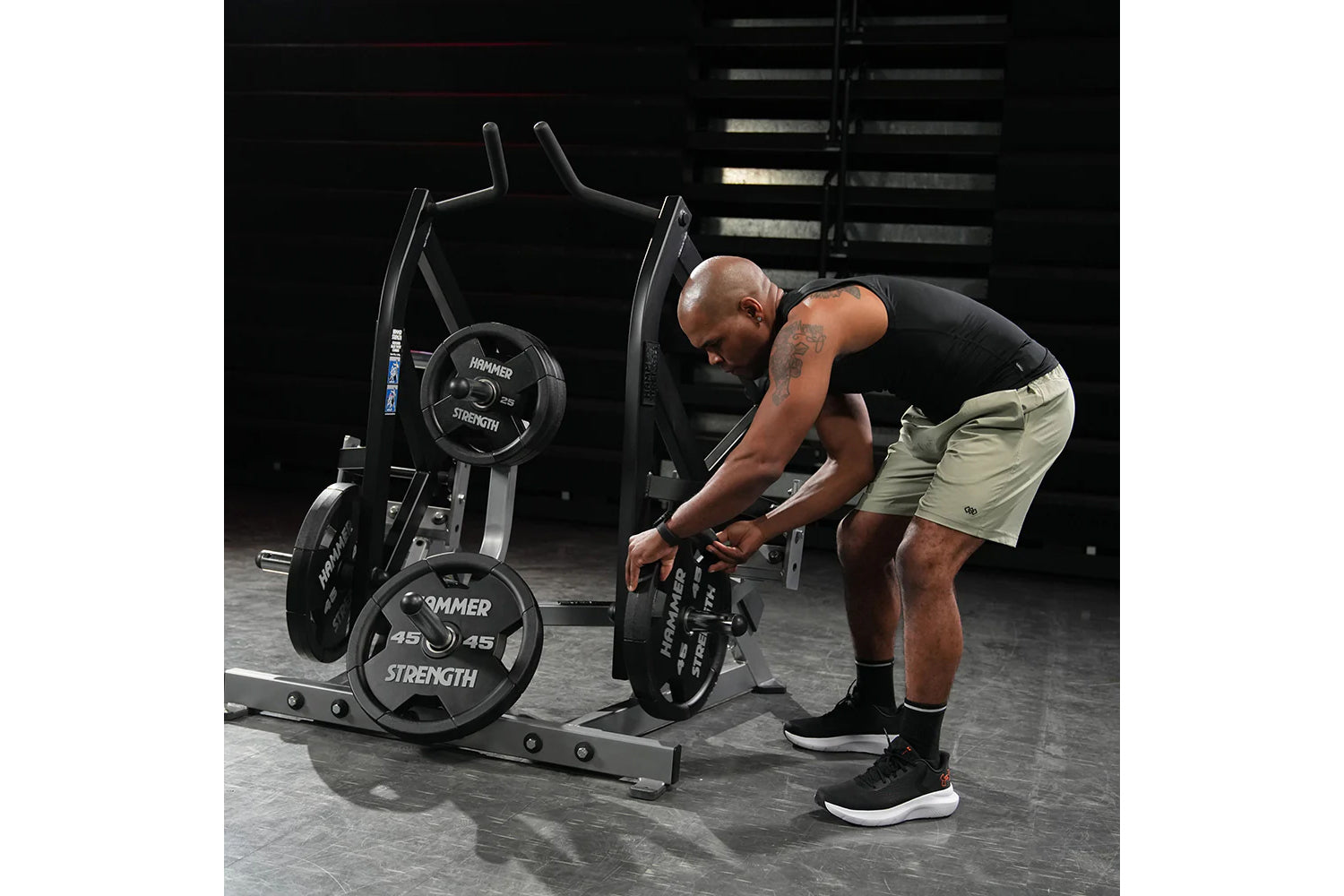 Man using black Hammer Strength plate-loaded combo twist machine in gym setting, wearing black sleeveless shirt and tan short