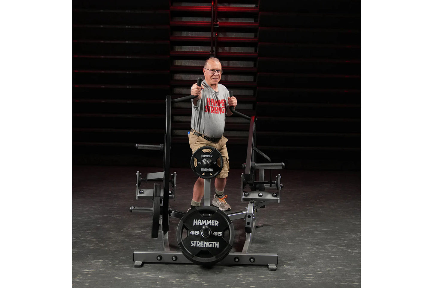 Man wearing gray t-shirt and tan shorts performing a twist exercise on black Hammer Strength plate-loaded machine in gym sett