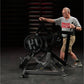 Man wearing gray Hammer Strength t-shirt using black plate-loaded exercise machine with weighted wheel in gym setting