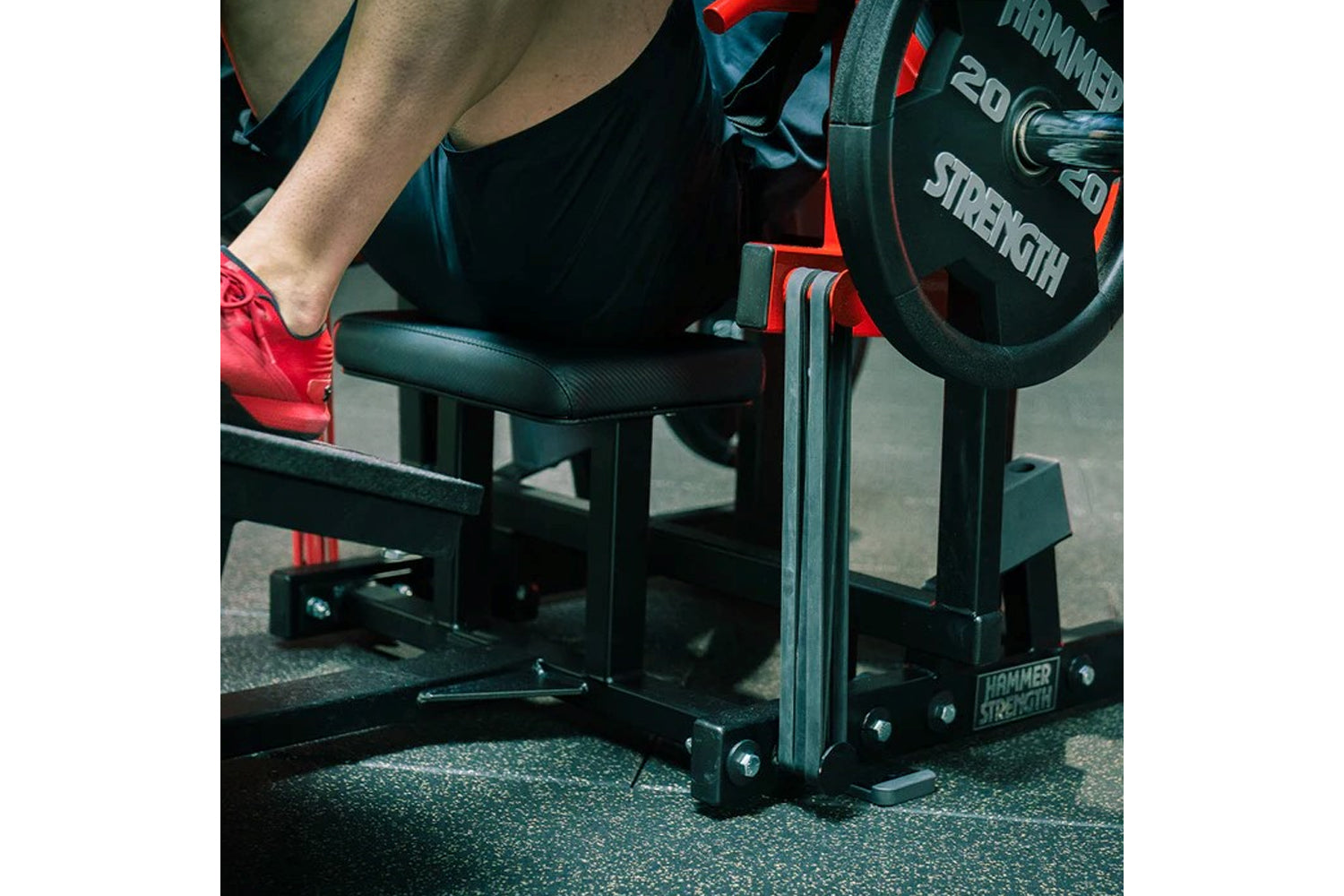 Person wearing red shoes using black Hammer Strength plate-loaded glute drive machine in gym setting