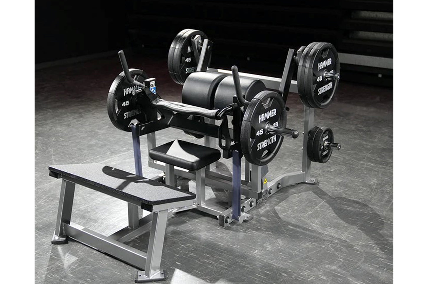 Hammer Strength plate-loaded glute drive machine with black 45-pound weight plates and silver frame on gym floor