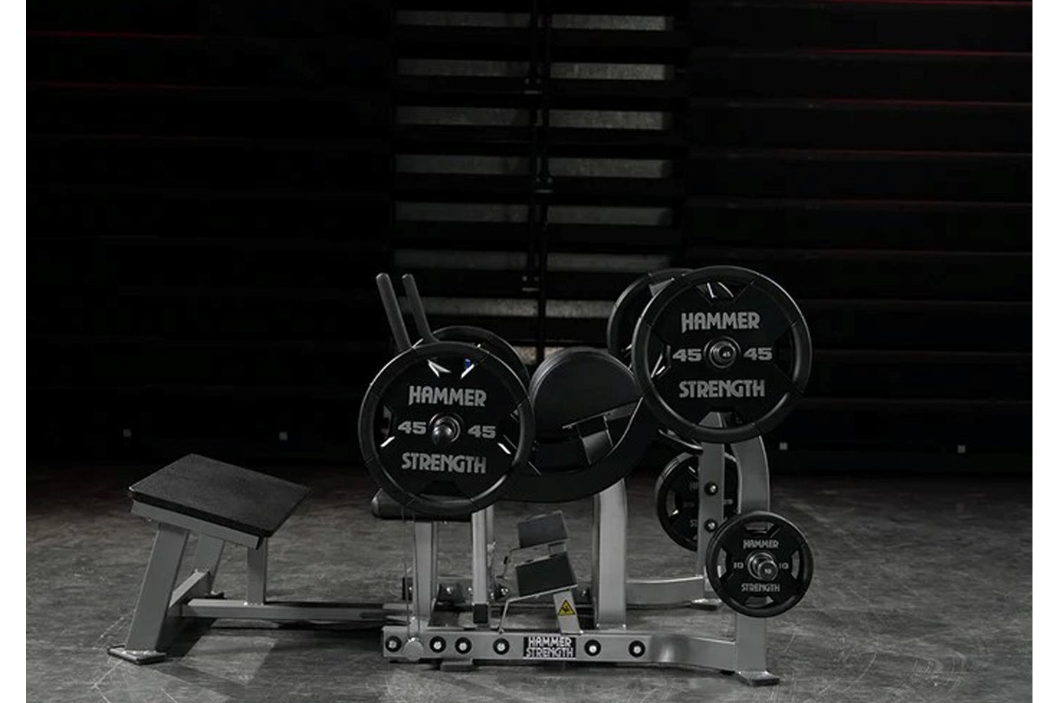 Hammer Strength plate-loaded glute drive machine with black weight plates and metal frame in gym setting