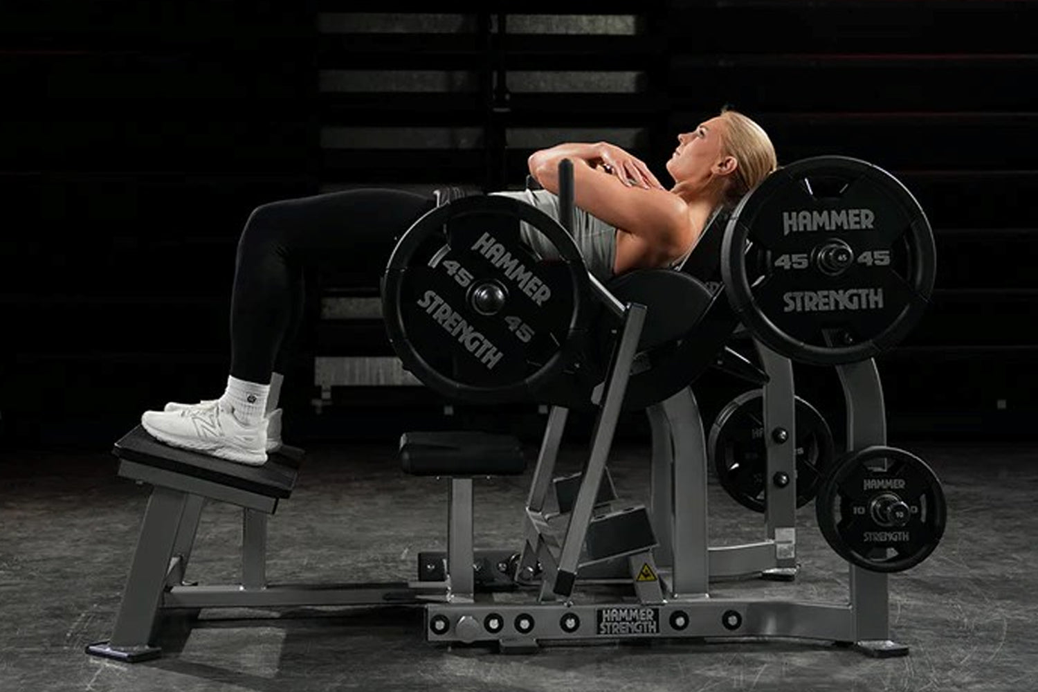 Woman performing chest press exercise on Hammer Strength plate-loaded machine with 45-pound weight plates in gym setting