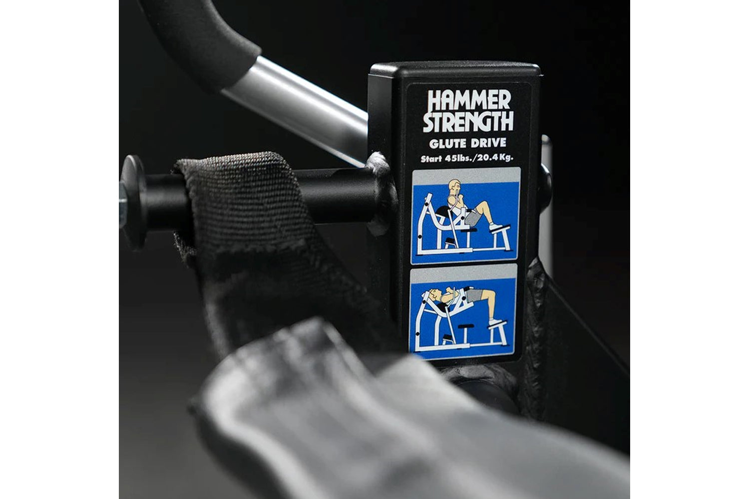 Hammer Strength Glute Drive plate-loaded machine with black box packaging and blue instructional graphics, surrounded by weig