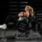 Woman using black Hammer Strength plate-loaded glute drive machine with loaded weight plates in gym setting
