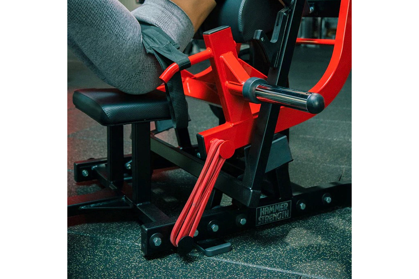 Red and black Hammer Strength plate-loaded glute drive machine with padded seat, used by model in gym setting