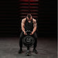 Man in black tank top and pants using Hammer Strength plate-loaded gripper in gym setting with red metal stairs background