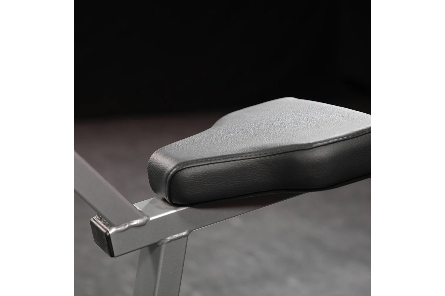 Black padded vinyl seat with chrome base on dark background, detail view of Hammer Strength Plate-Loaded Gripper