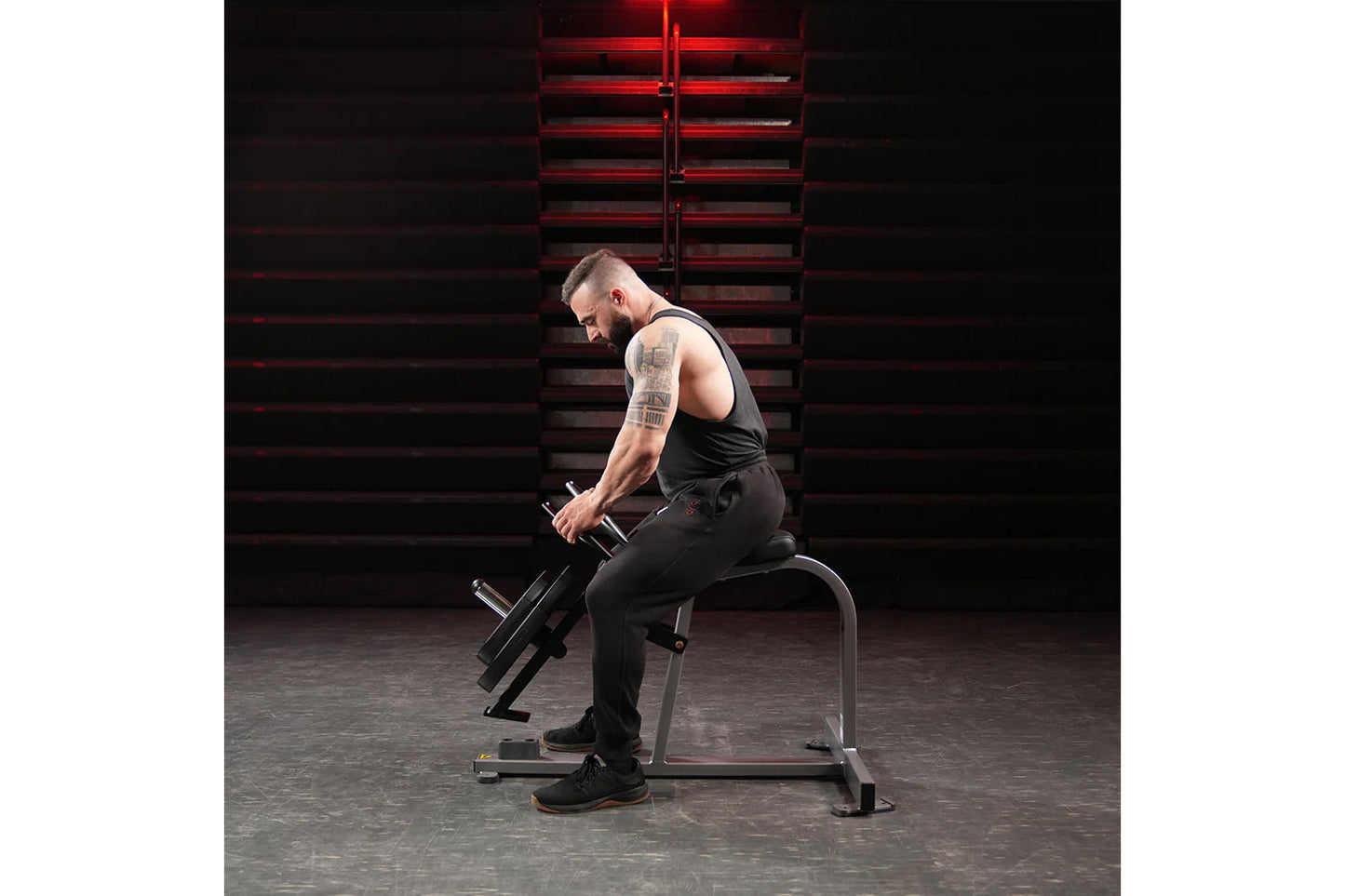 Man seated on weight bench performing dumbbell curl exercise in industrial gym setting with red neon lighting