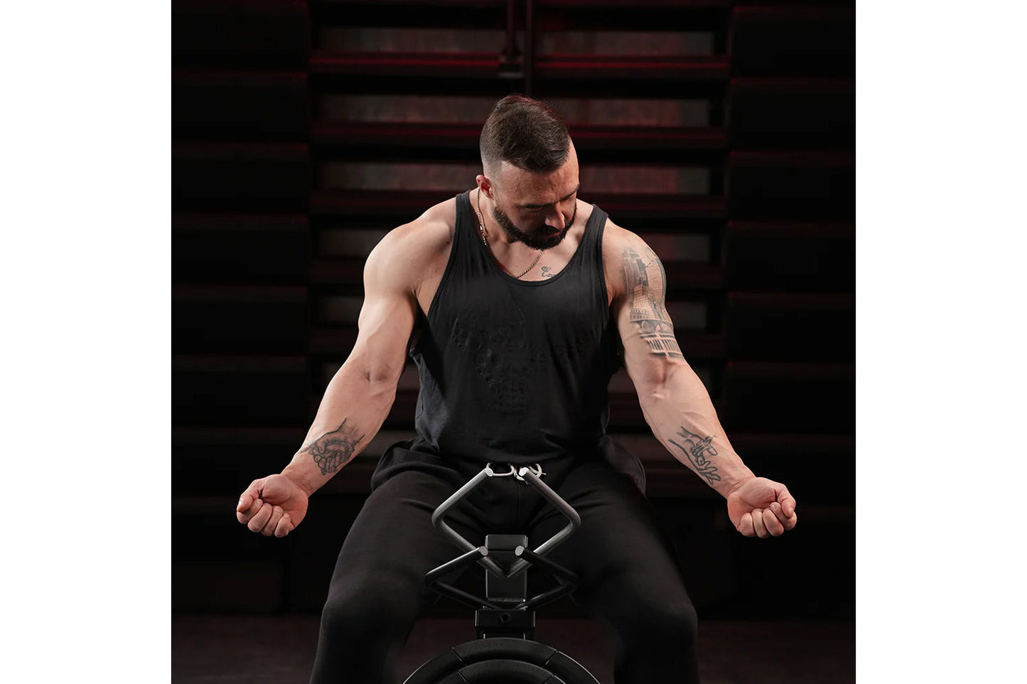 Man wearing black tank top and black pants using plate-loaded gripper machine with industrial staircase background