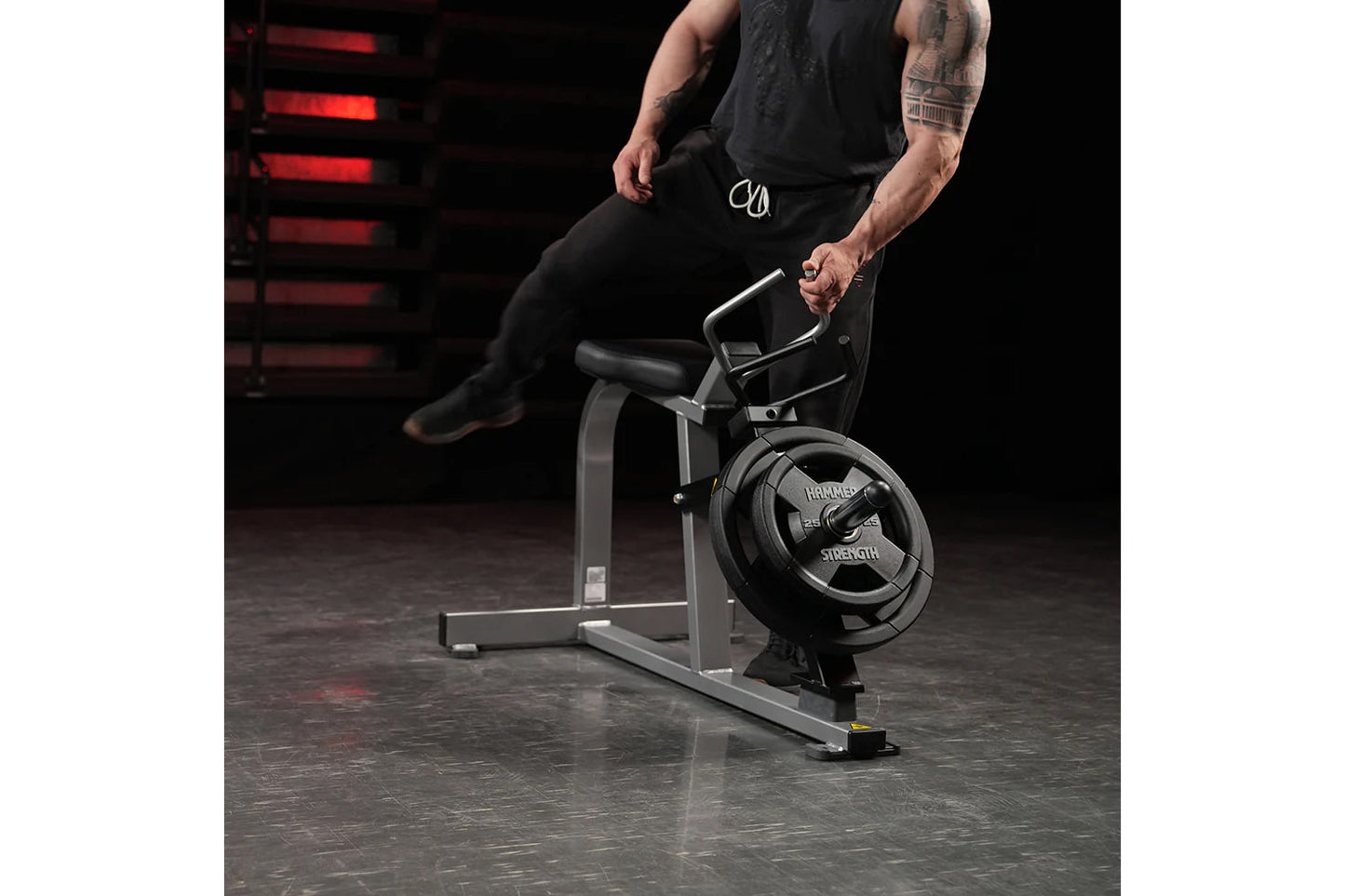 Man in black athletic wear seated on Hammer Strength plate-loaded leg press machine in gym setting with red neon lighting