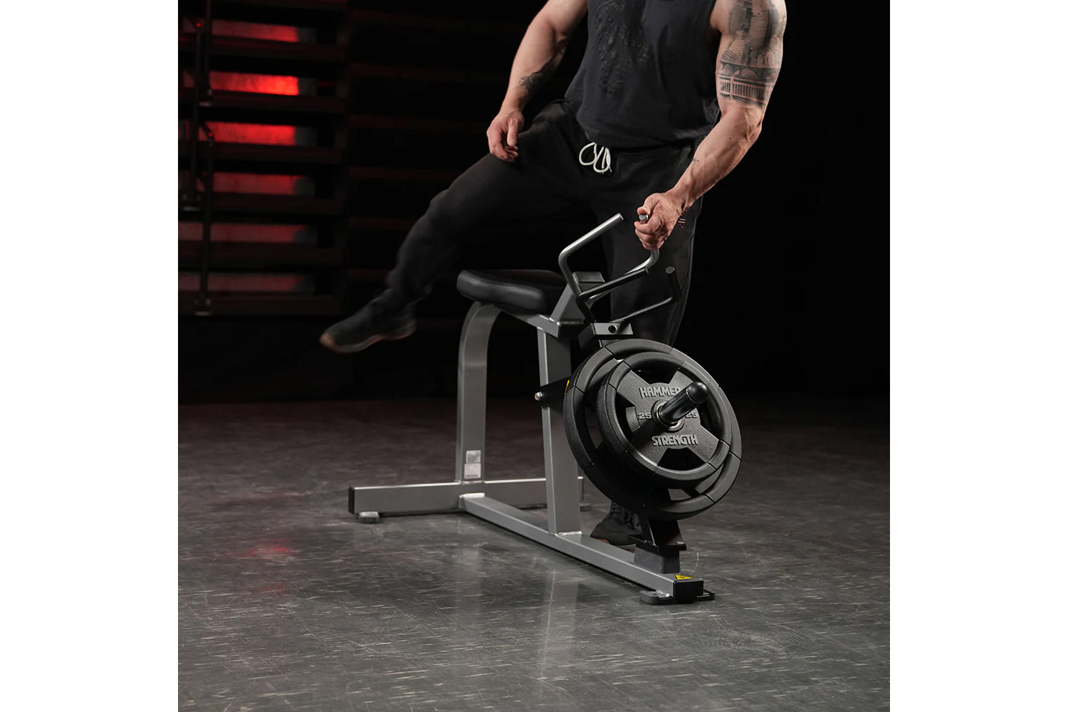 Man in black athletic wear seated on Hammer Strength plate-loaded leg press machine in gym setting with red neon lighting