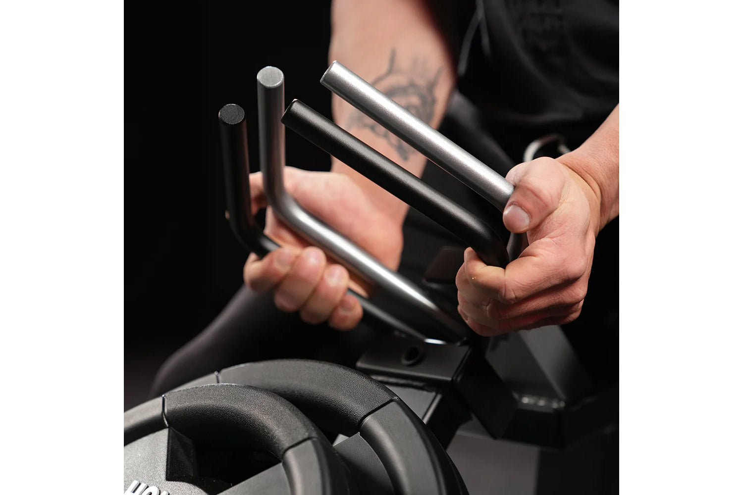 Person holding two plate-loaded grippers with black handles and metal cylinders against black background