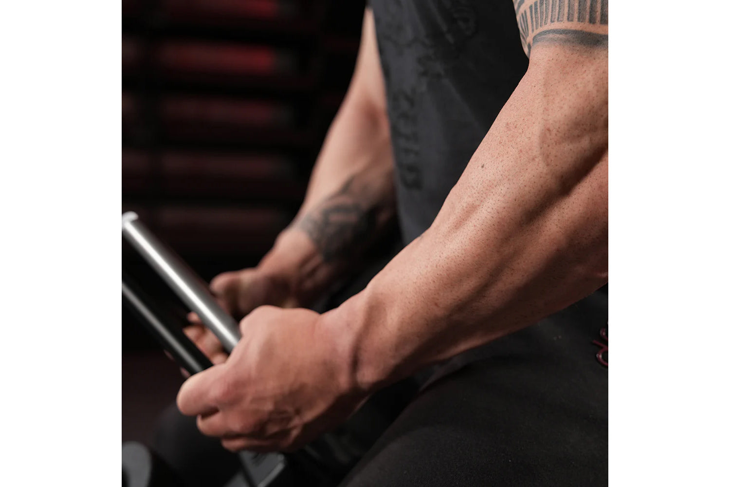 Person with tattooed arms wearing black long-sleeve shirt, holding metal plate-loaded gripper exercise equipment