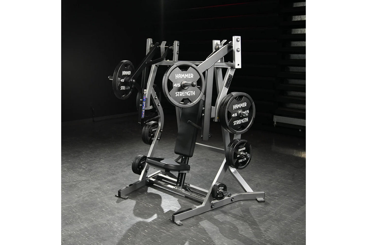 Hammer Strength plate-loaded iso-lateral bench press with silver frame, black seat, and loaded weight plates on gym floor