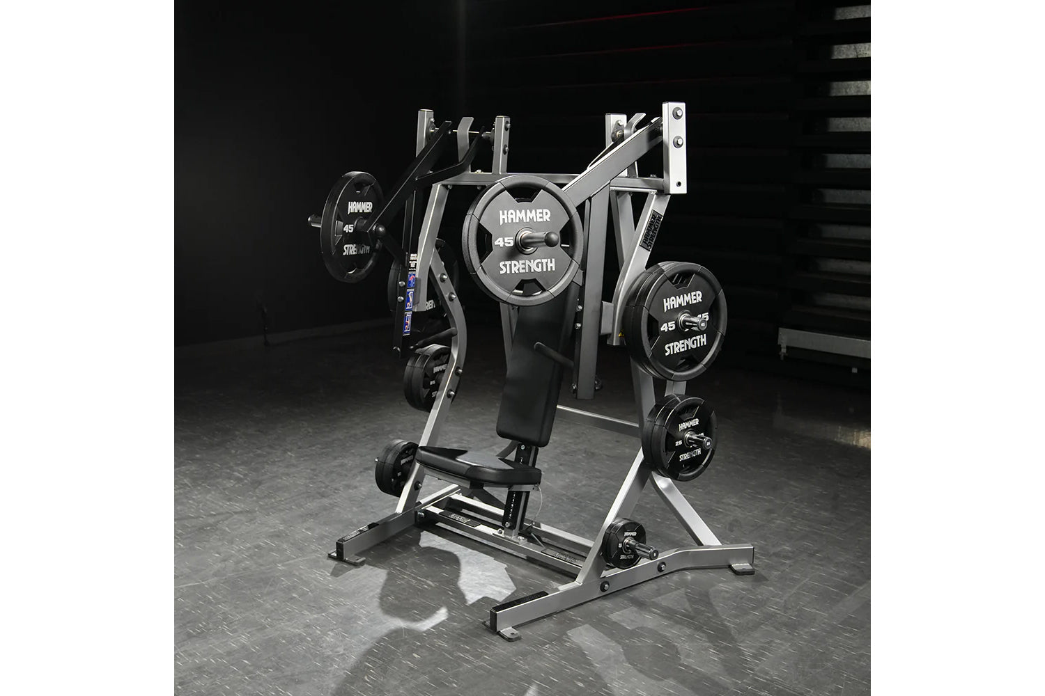 Hammer Strength plate-loaded iso-lateral bench press with silver frame, black seat, and loaded weight plates on gym floor
