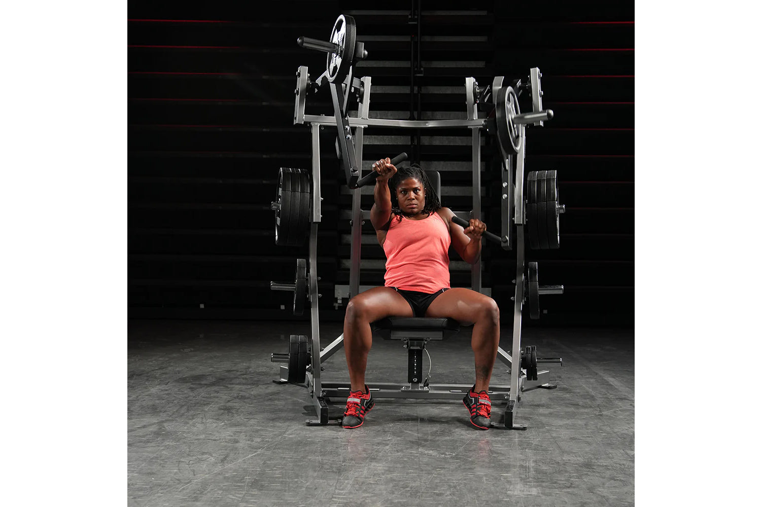 Athlete wearing coral tank top and black shorts performing bench press on Hammer Strength plate-loaded machine in gym setting