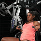 Woman in coral tank top using silver and black Hammer Strength plate-loaded bench press machine with loaded barbell