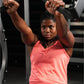Woman wearing coral sleeveless tank top using plate-loaded bench press machine in gym setting
