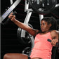 Woman in coral tank top using Hammer Strength plate-loaded bench press machine in gym setting