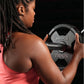 Woman in pink tank top holding black and gray Hammer Strength 25-pound dumbbell against black background