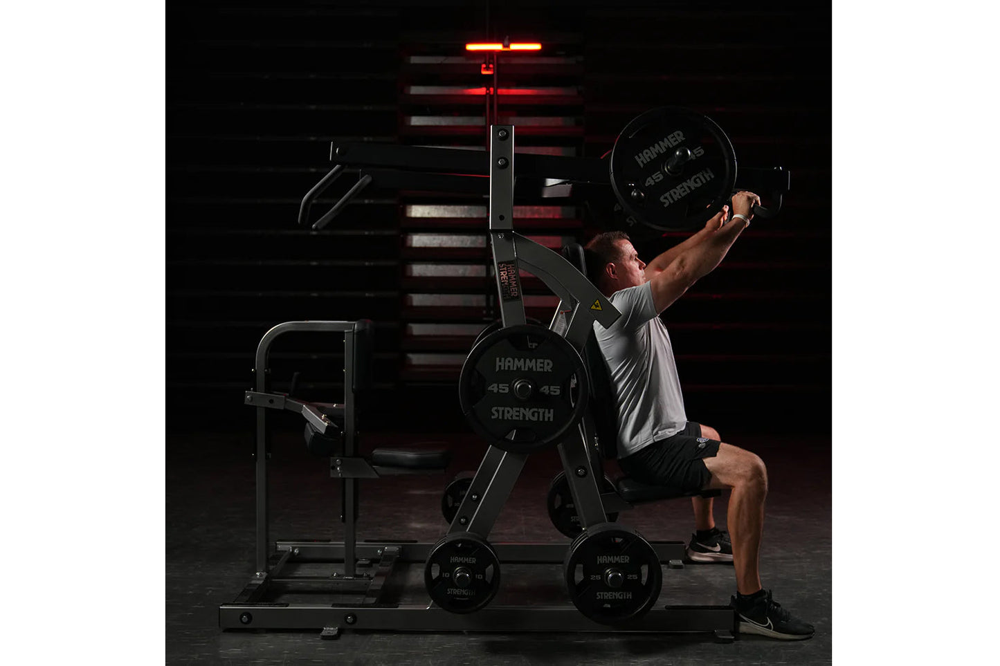 Man performing chest press on Hammer Strength black plate-loaded machine in gym with red lighting overhead