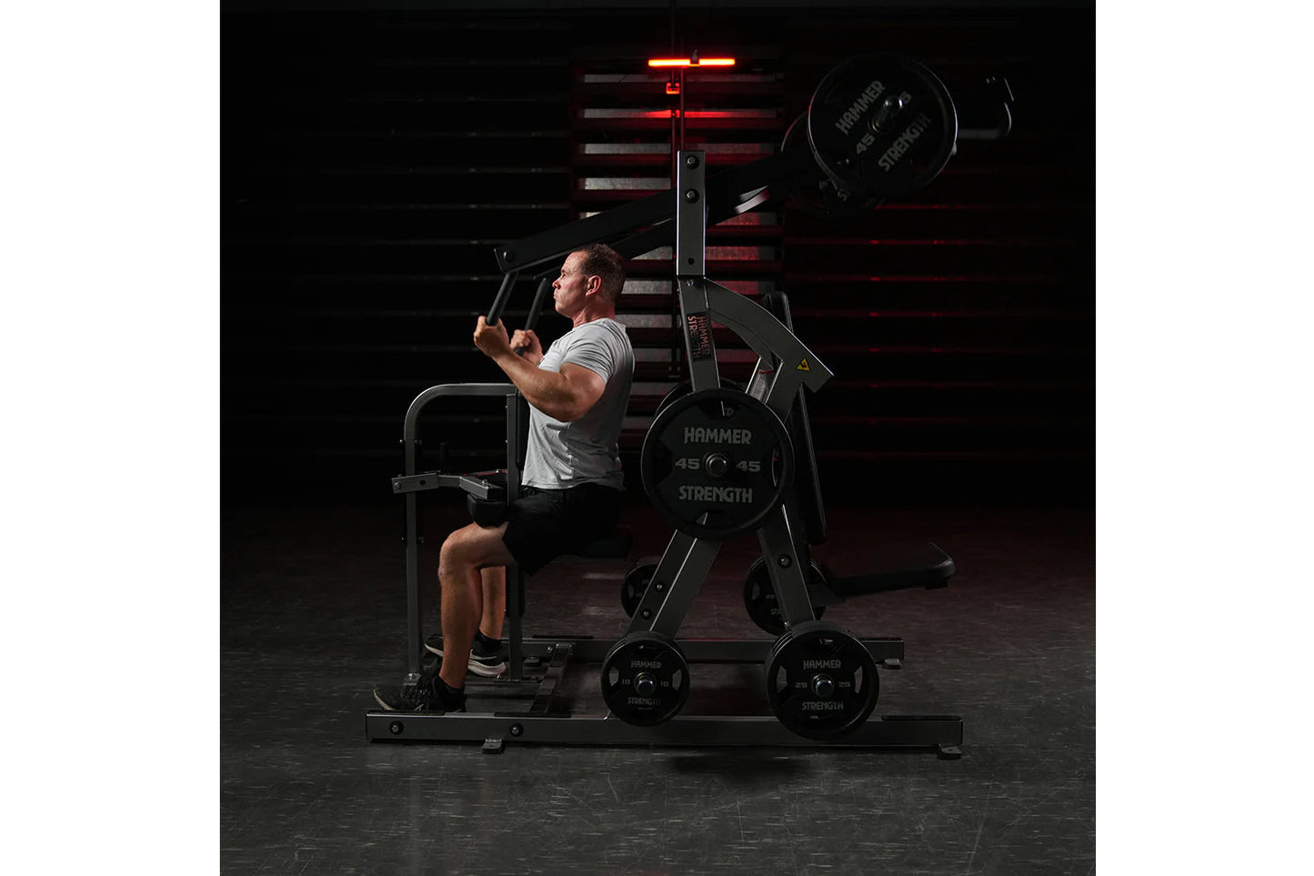 Man using black Hammer Strength plate-loaded chest/back machine in gym setting with red accent lighting