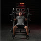 Man wearing gray Hammer Strength t-shirt and black shorts using plate-loaded chest machine in gym with red lighting