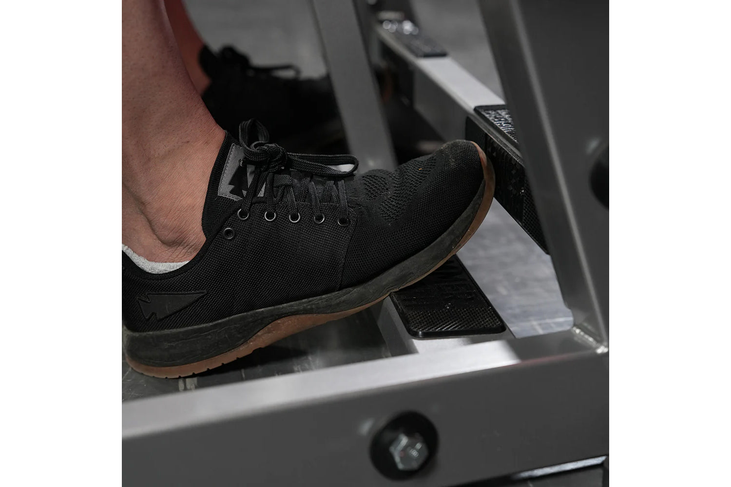Black mesh lace-up sneaker with brown sole, worn by model on exercise equipment