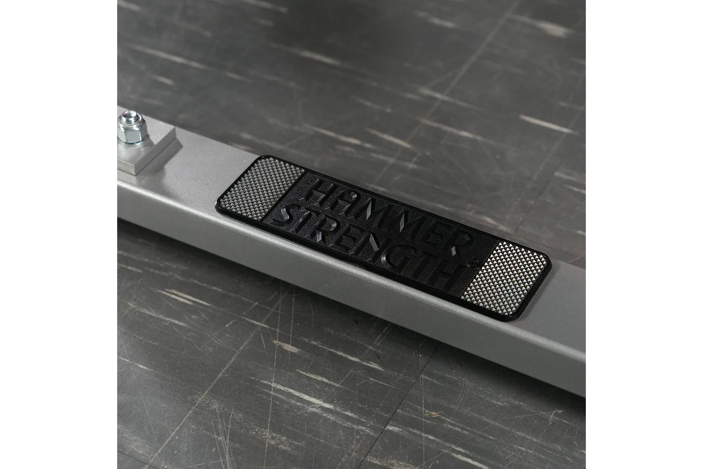 Black and silver textured plate-loaded row machine nameplate on white ledge with dark tile background