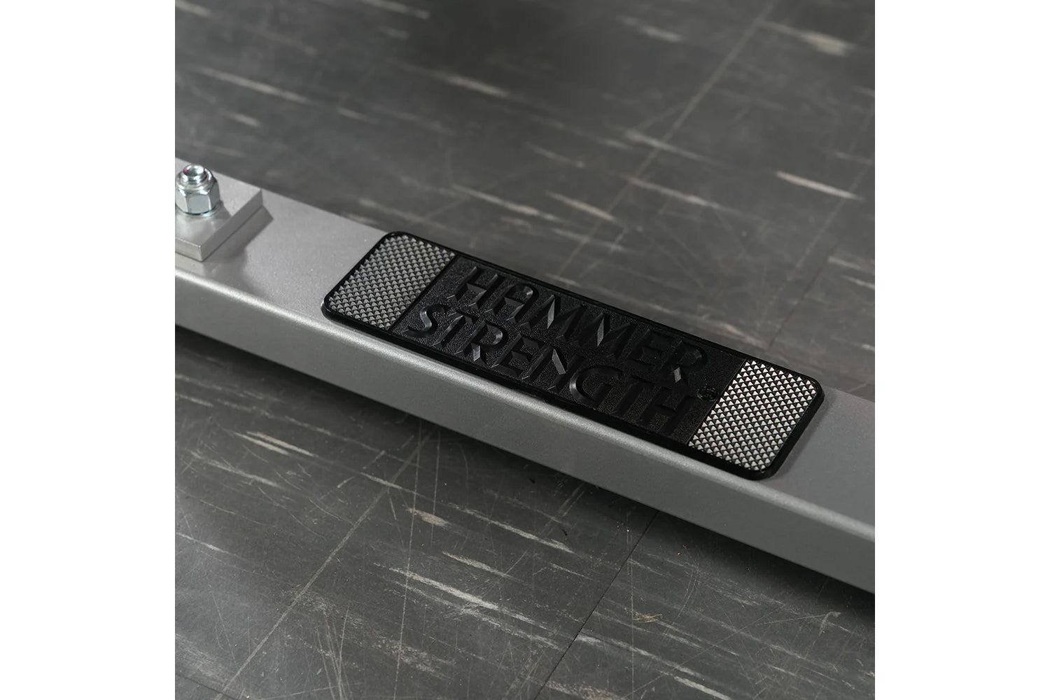 Black and silver textured plate-loaded row machine nameplate on white ledge with dark tile background