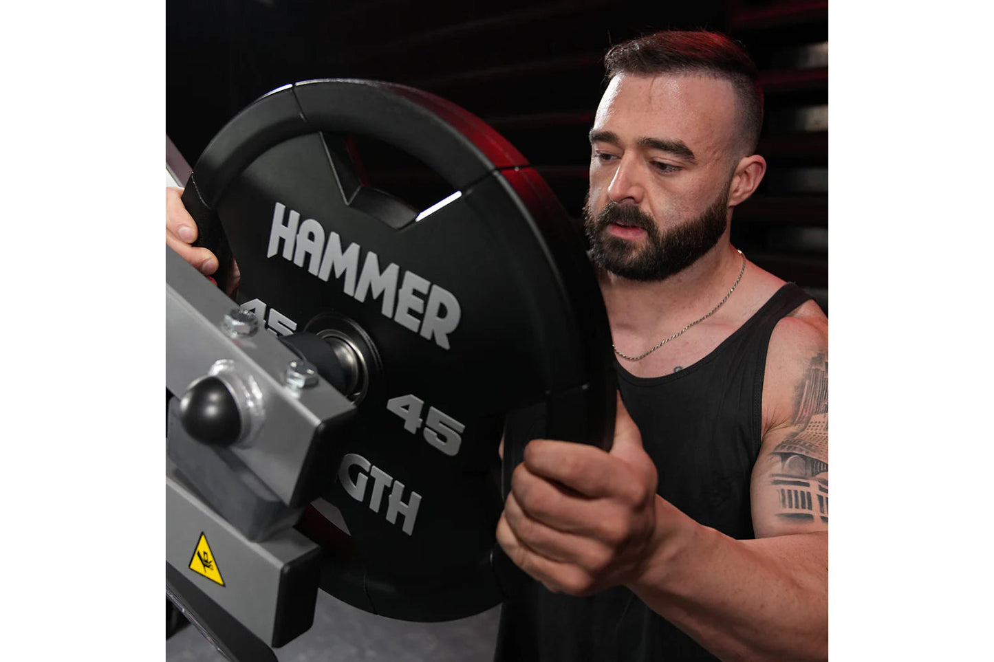 Man using black Hammer Strength plate-loaded rowing machine with 45-pound weight plates loaded, worn by model in black tank t