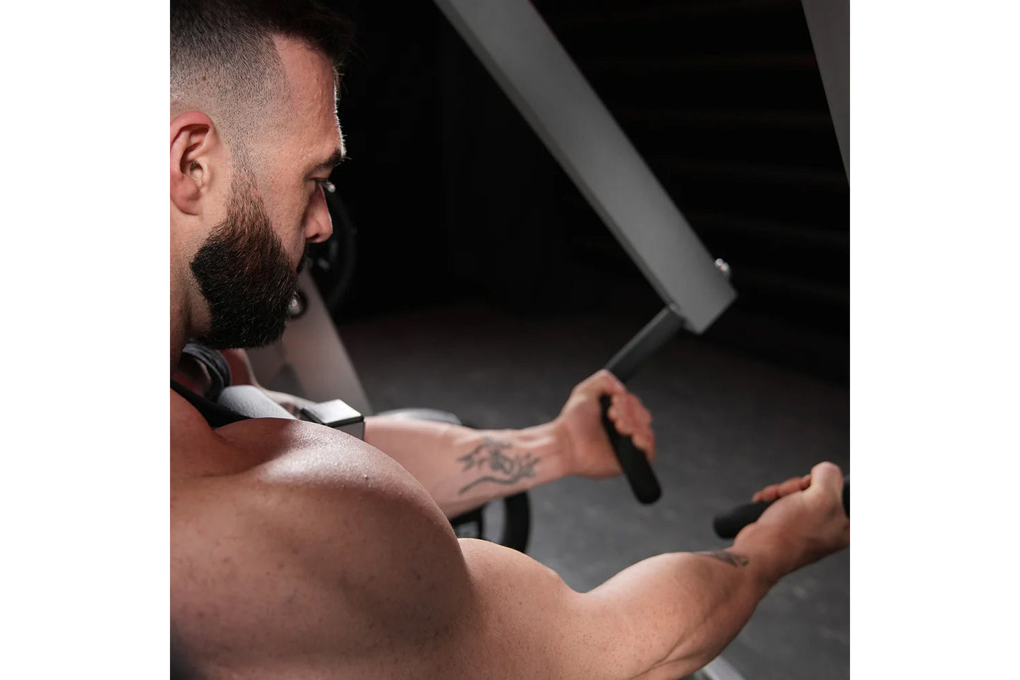 Bearded man with tattoos using plate-loaded iso-lateral row machine in gym setting