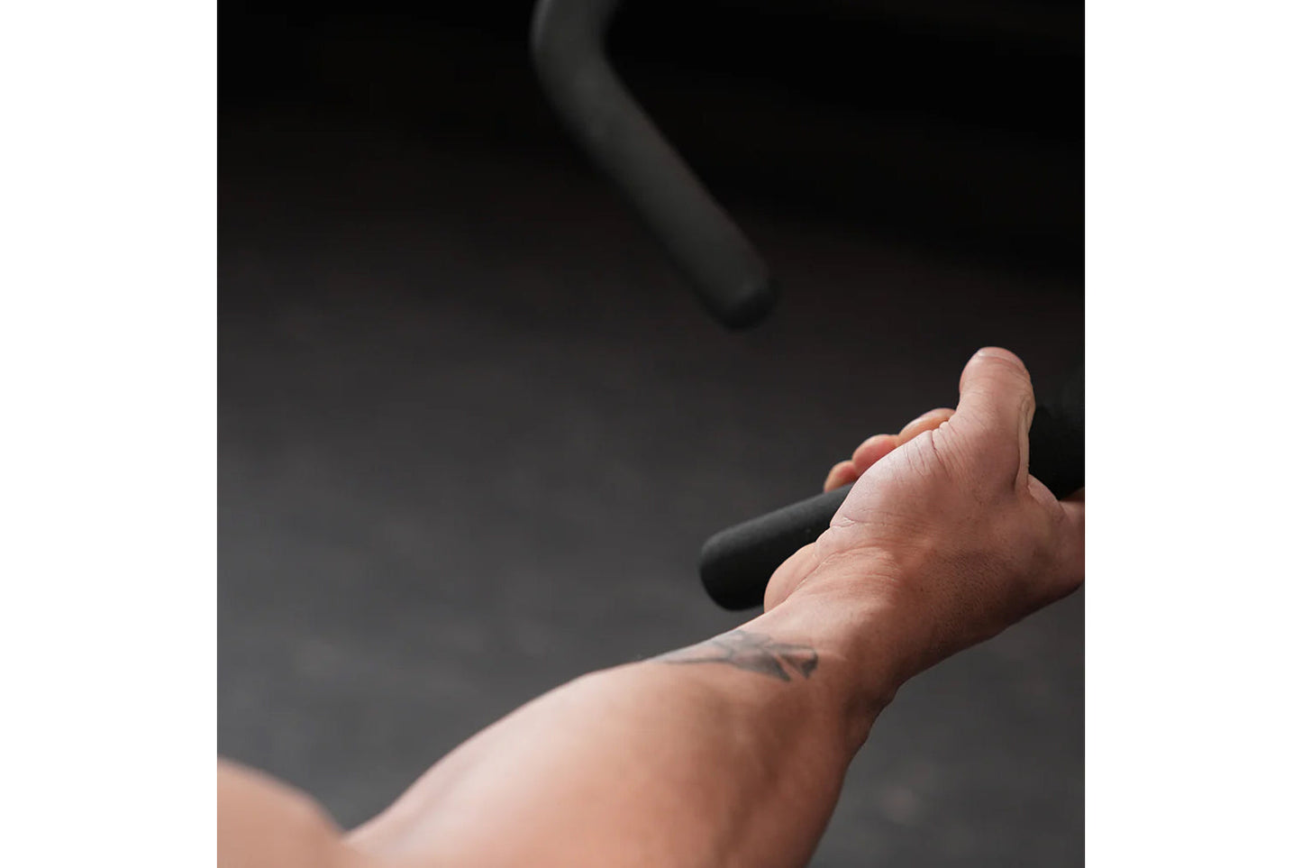 Hand gripping black handle of plate-loaded row machine against dark background