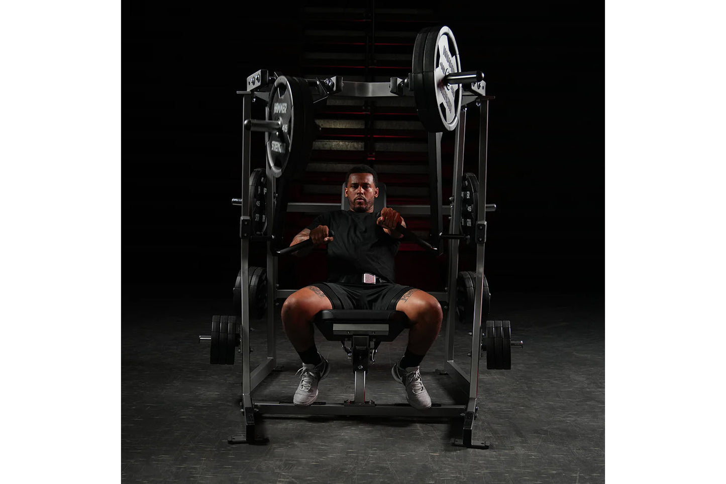 Man wearing black shirt and shorts using Hammer Strength plate-loaded decline chest press machine with loaded weight plates i