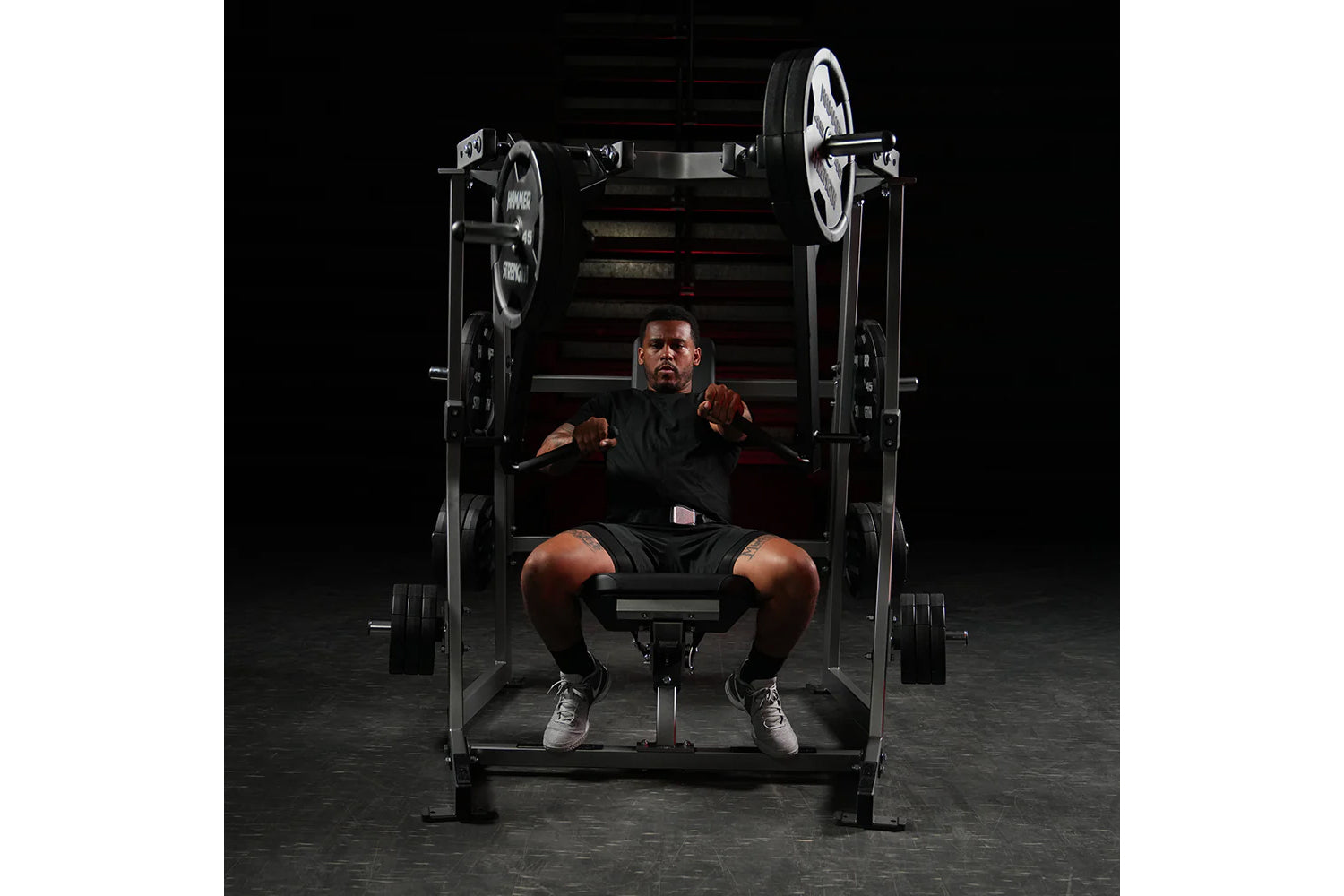 Man wearing black shirt and shorts using Hammer Strength plate-loaded decline chest press machine with loaded weight plates i