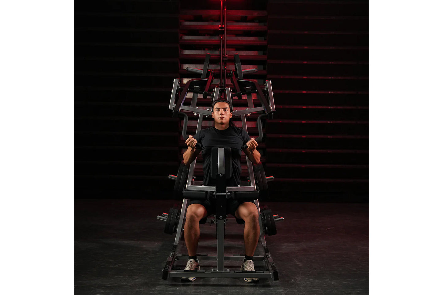 Man using black and red plate-loaded lat pulldown machine in gym setting with red lighting backdrop